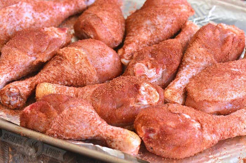 raw chicken drumsticks coated with dry rub on the metal sheet pan