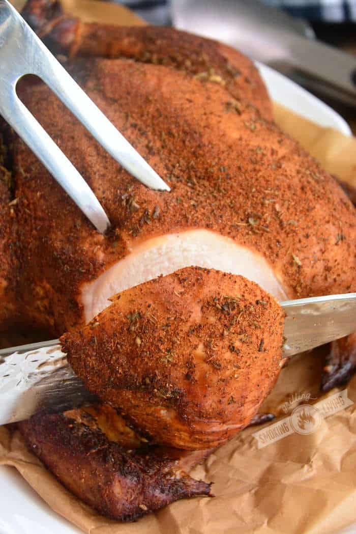 slicing into the smoked chicken breast with a knife and holding with a fork