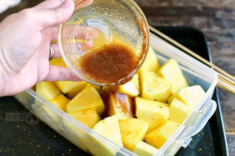 pouring brown sugar mixture over pineapple chunks in a plastic container