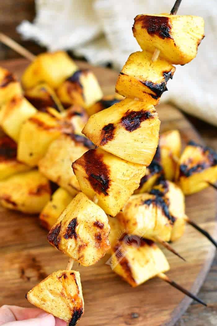 holding a skewer of grilled pineapple chunks