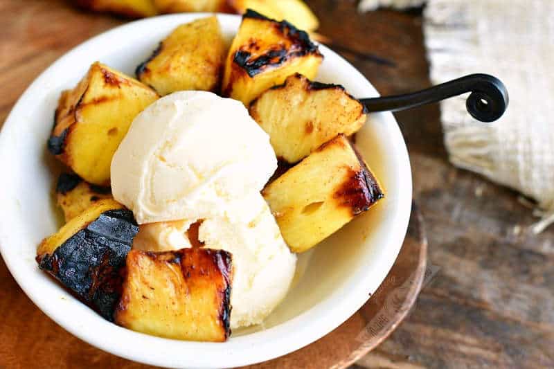 bowl of vanilla ice cream and grilled pineapple chunks with a black spoon
