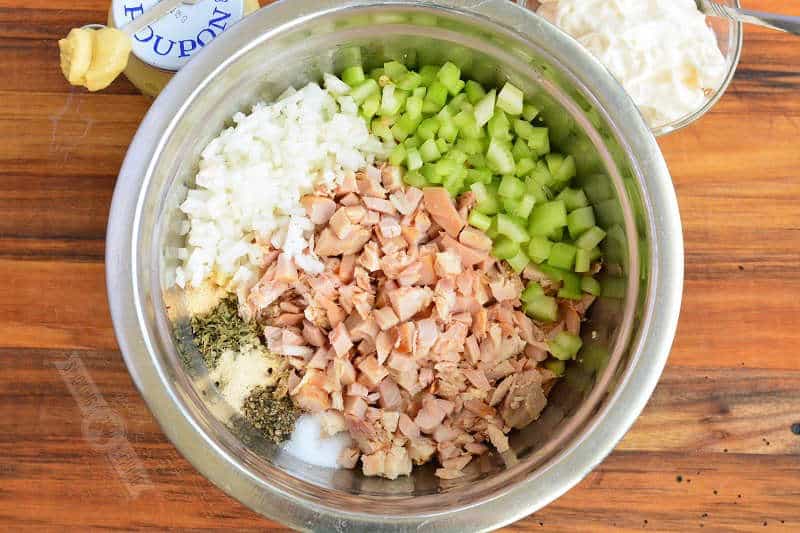 diced chicken, celery, onion, and seasonings in a mixing bowl with mayo and mustard next to a bowl