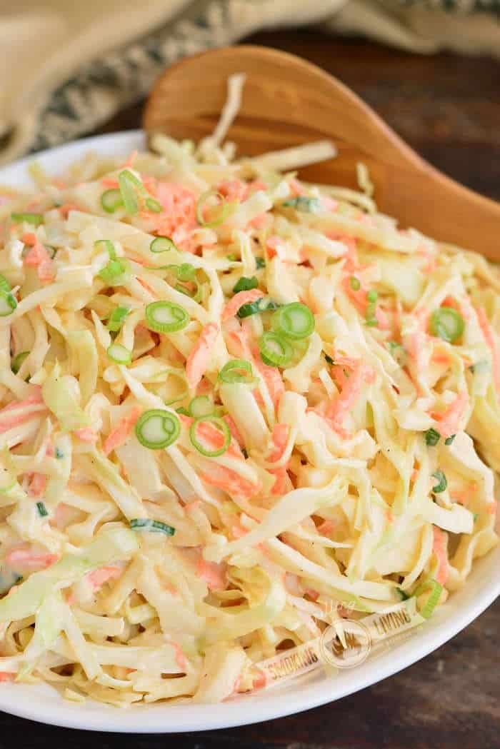 side view of coleslaw in a bowl with wooden spoon in the bowl