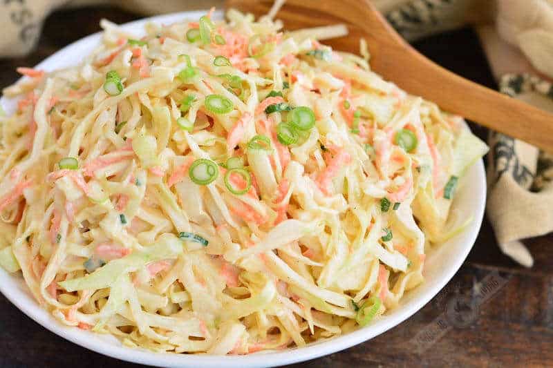 horizontal view of coleslaw in a bowl with a wooden spoon next to it