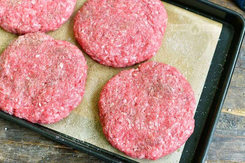 four raw burger patties on a black tray and parchment paper