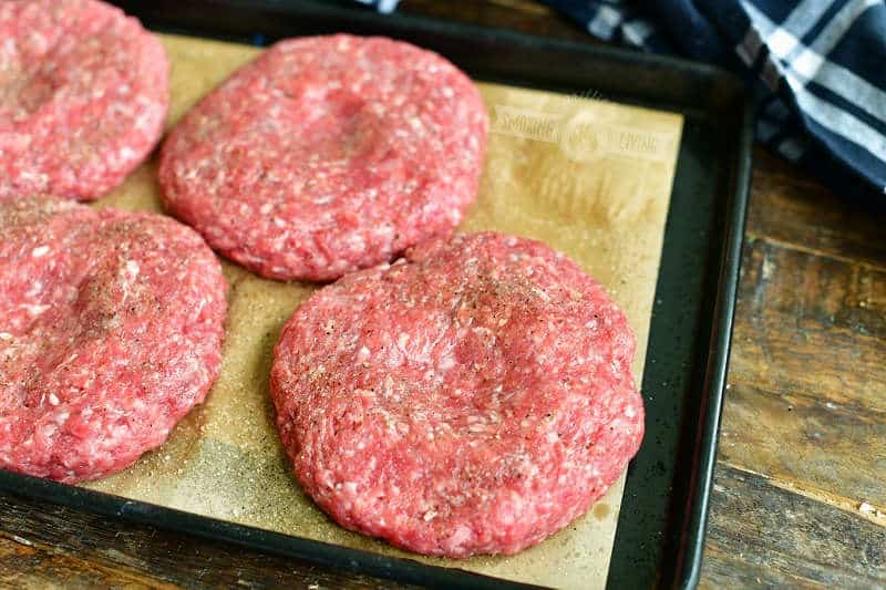 raw burger patties on a baking sheet on parchment paper with a small well imprint in the middle