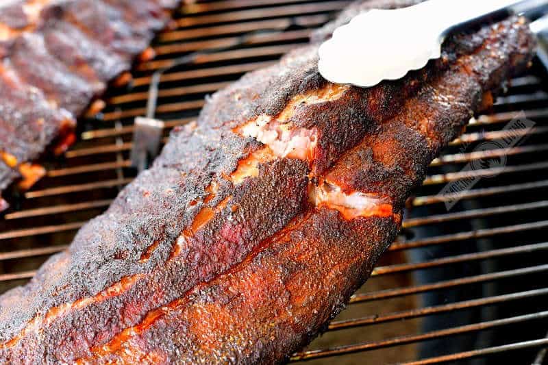 pulling a rack of ribs off the smoked with metal tongues and the rib meat cracking