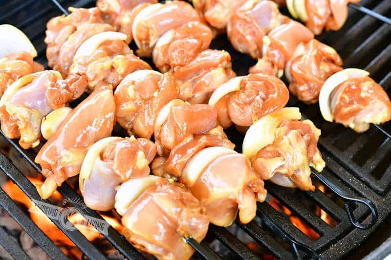 uncooked chicken and onions skewered on black skewers on the grill