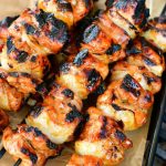 skewers of cooked chicken pieces on a black tray with parchment paper