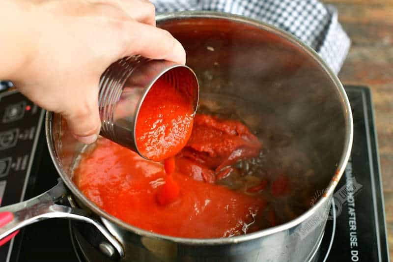 pouring tomato sauce into the pot with other ingredients