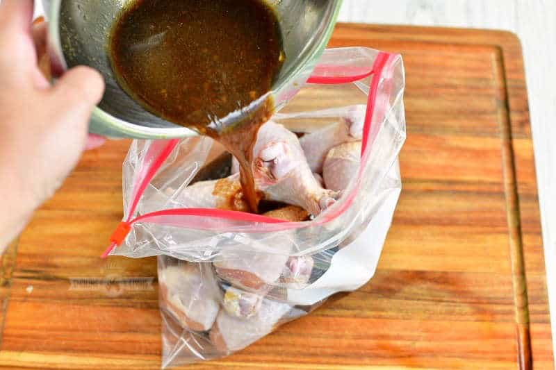 pouring the marinade out of a mixing bowl into a zip lock bag with chicken legs