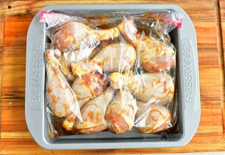 chicken legs in a bag with marinade inside a metal bake pan on a wooden board