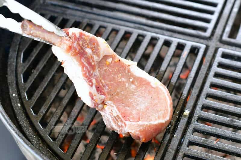 placing a raw marinated pork chop onto the hot grill using tongs