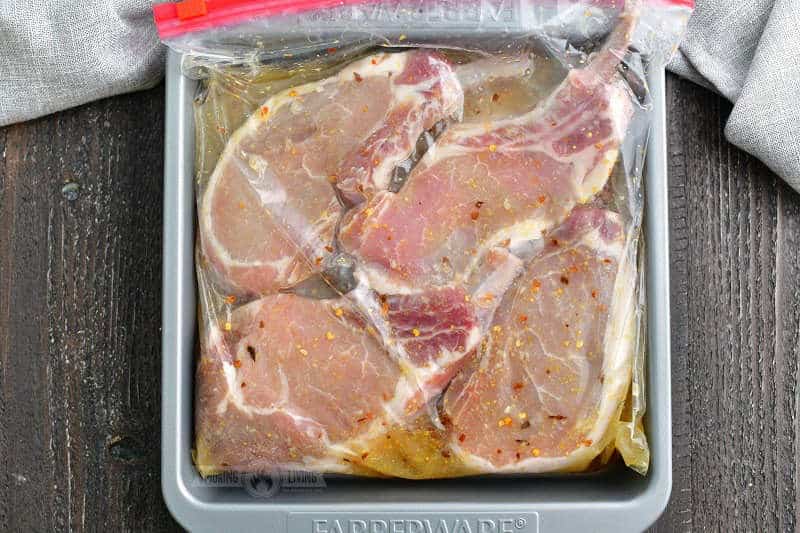four pork chops with bones in a yellowish marinade in a zip-top back inside a metal baking pan