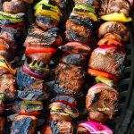 four long skewers with cooked steak pieces and vegetables skewered onto them on the grill
