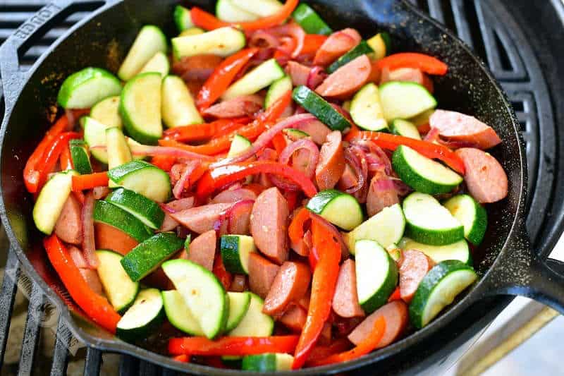 uncooked vegetables and sausage mixed together in a cast iron skillet on the grill