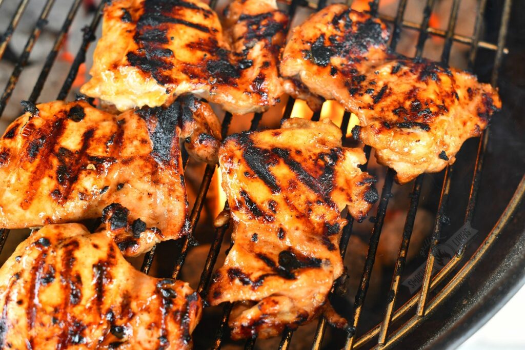 chicken cooking on the grill with charcoal visible below