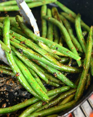 using metal tongs to scoop green beans in a skillet