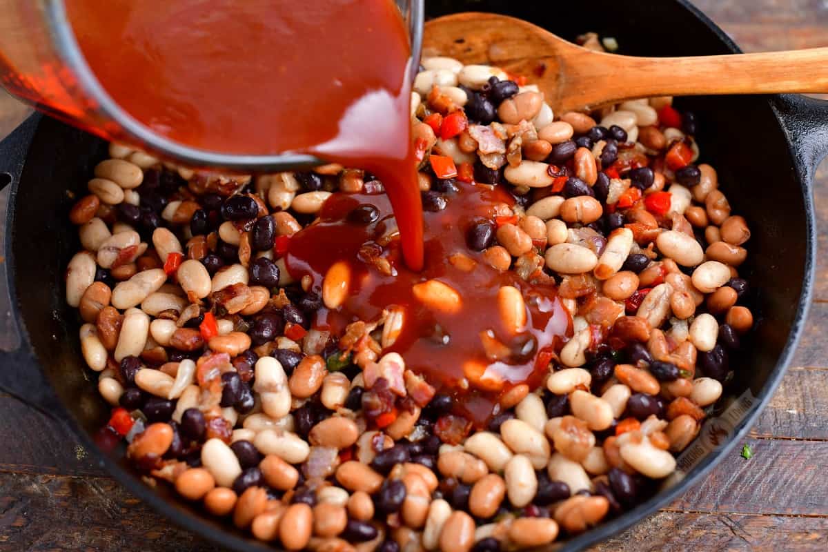 pouring bbq sauce into the skillet with mixed beans and vegetables