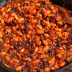 smoked beans in bbq sauce in a skillet with a wooden spoon