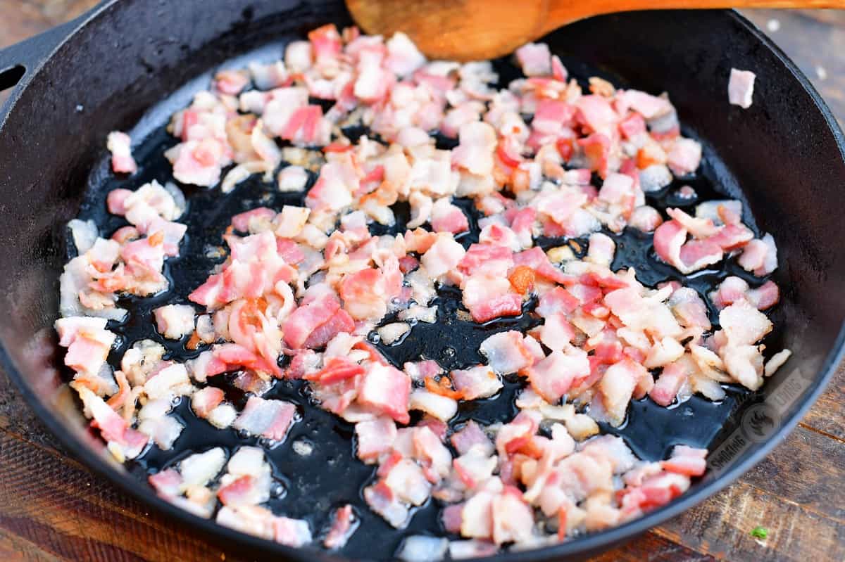 bacon pieces cooking in a cast iron skillet
