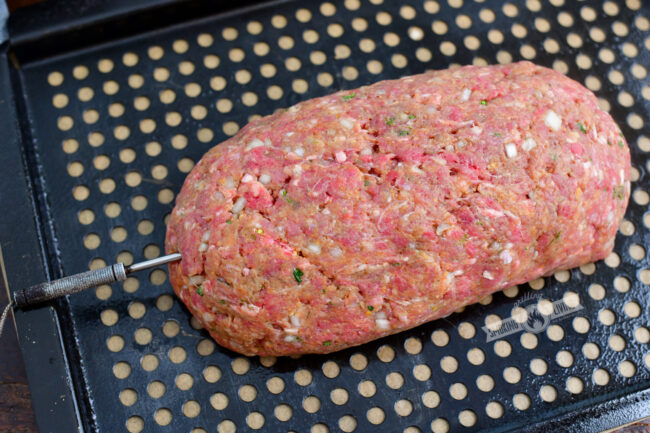 uncooked shaped meatloaf on a grill basket with thermometer
