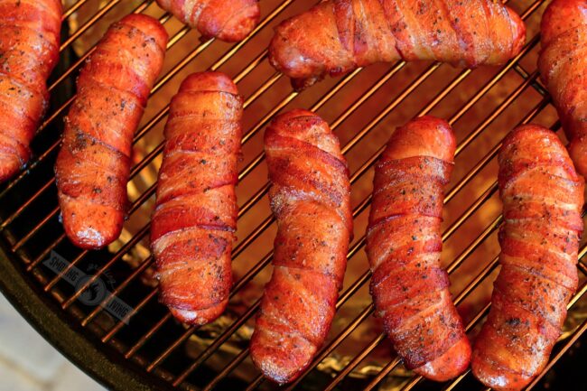 closeup of bacon wrapped sausage on a smoker grate