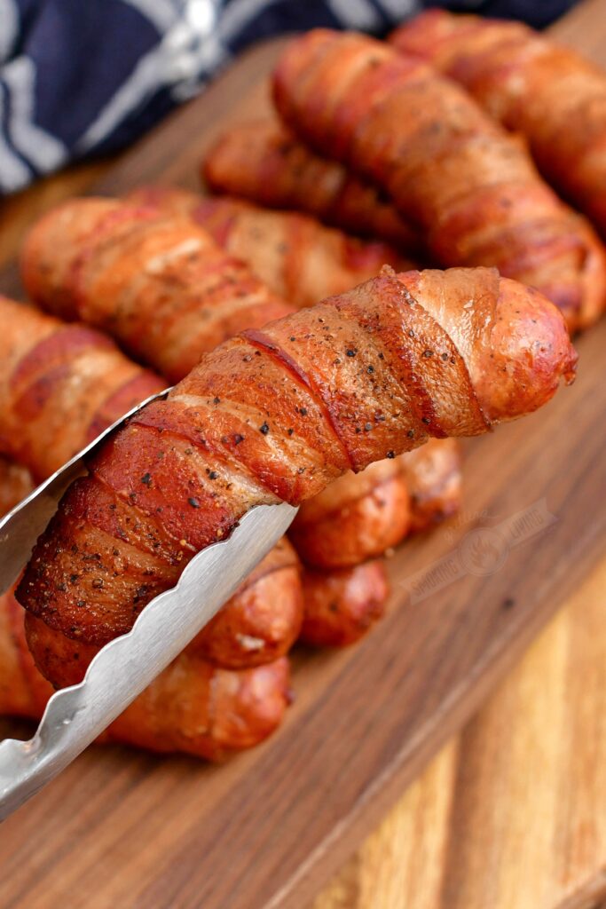 holding smoked sausage with metal tongs