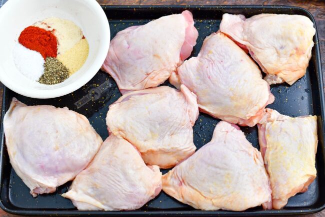 raw chicken thighs and seasoning in a bowl on a metal sheet tray