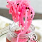 scooping pickled red onion strings from a glass jar