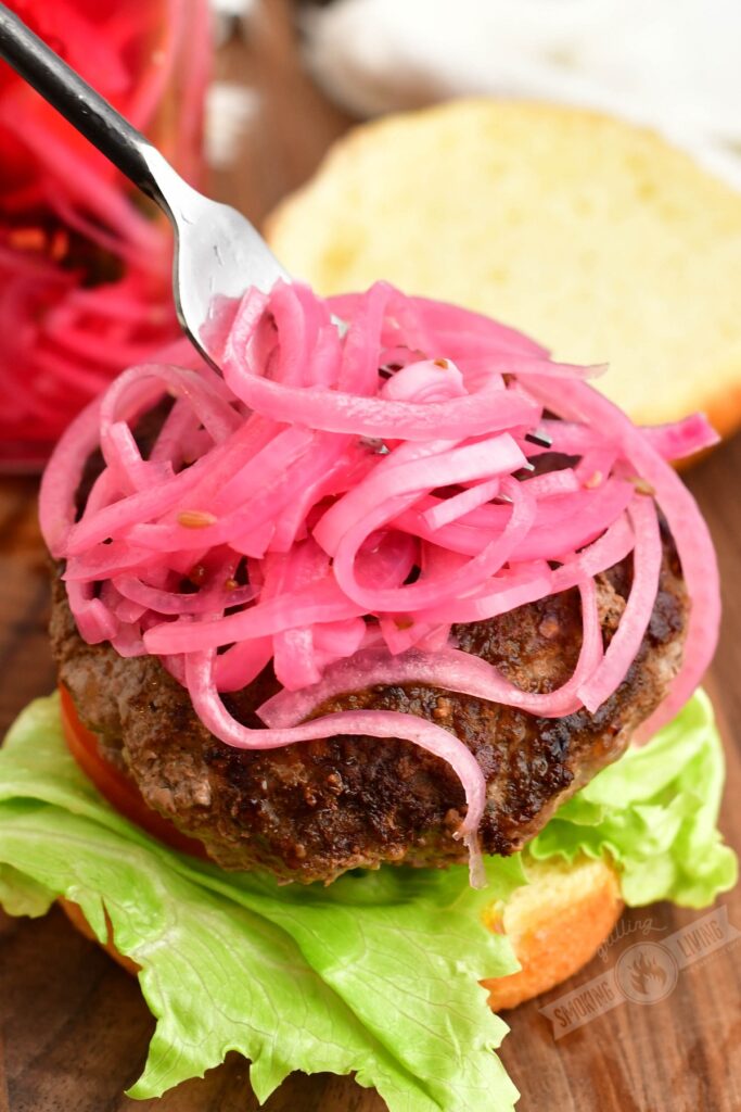topping a hamburger with picked red onions