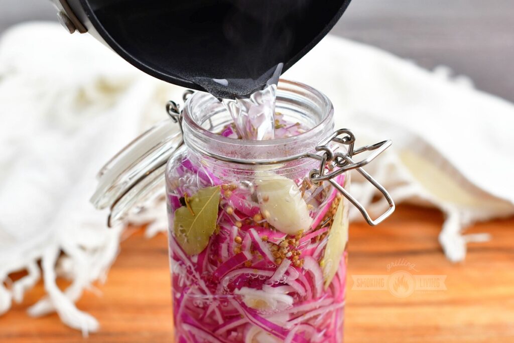 pouring in clear liquid into glass jar with red onions