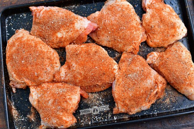 raw chicken thighs on a baking sheet with seasoning all over them