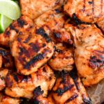 closeup of grilled chicken thighs and lime wedges on a metal pan