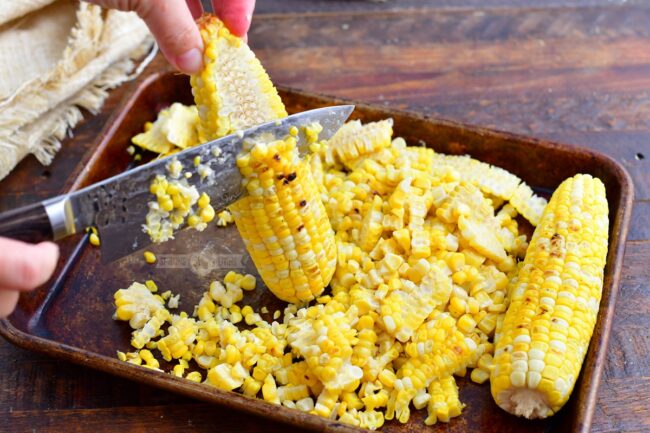cutting the kernels off of grilled corn on cob