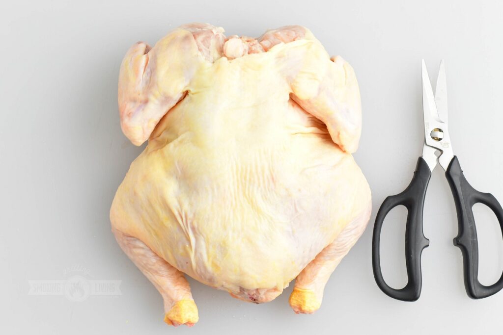 whole chicken on white cutting board with kitchen scissors next to it