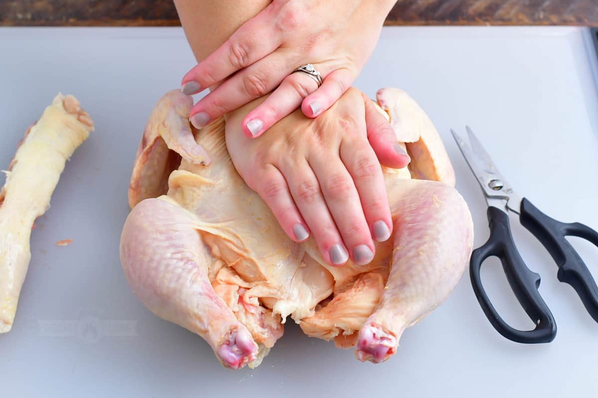 pushing on the breast of the whole raw chicken to help butterfly it