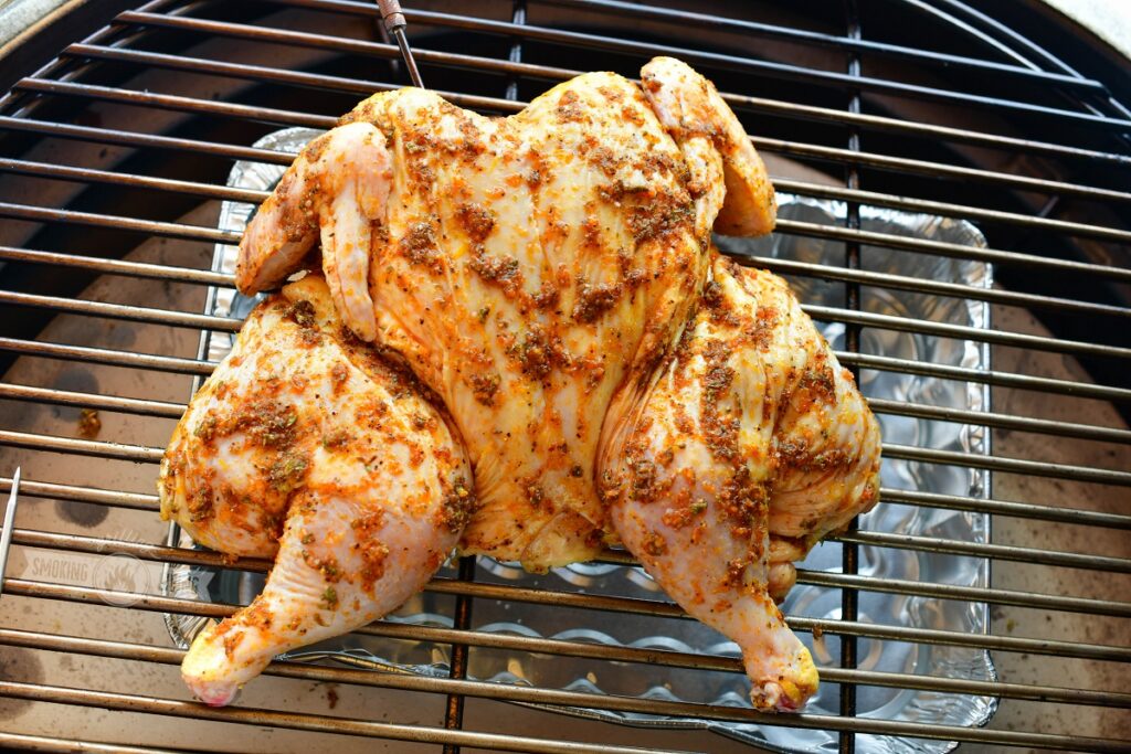 uncooked spatchcocked chicken on the grill with drip pan under