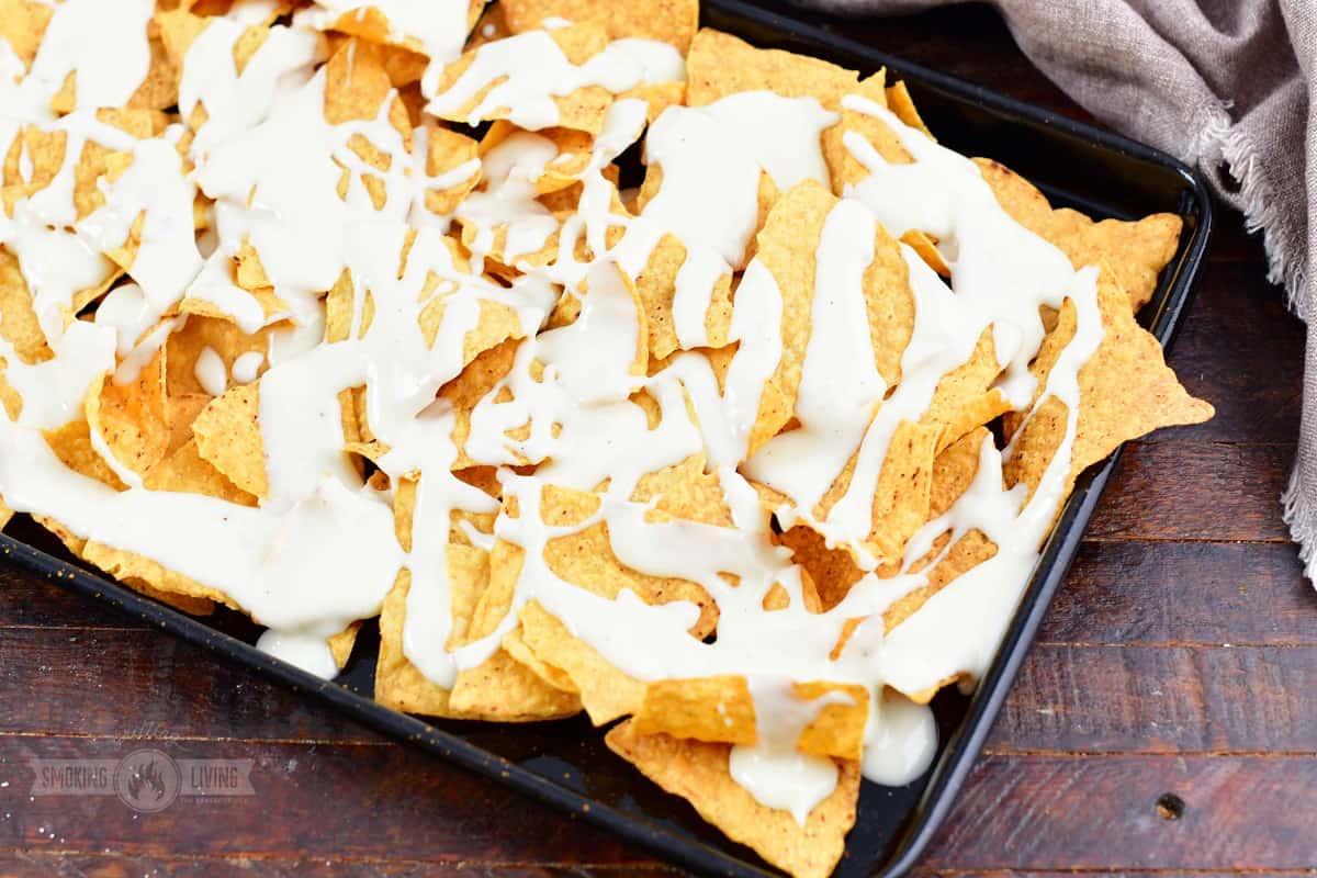 tortilla chips drizzled with queso on a baking sheet