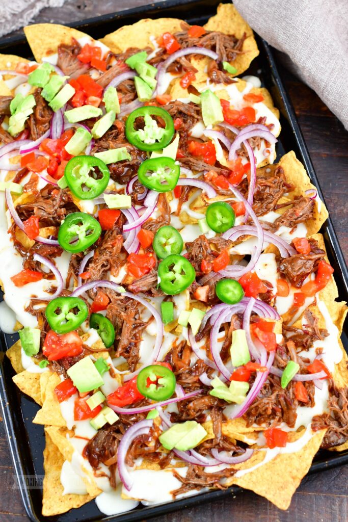 loaded beef nachos with queso on a baking sheet