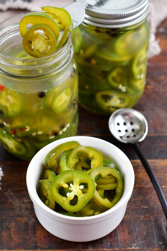 pickled jalapenos in a bowl next to jars