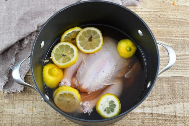 whole chicken brining in a pot with lemons