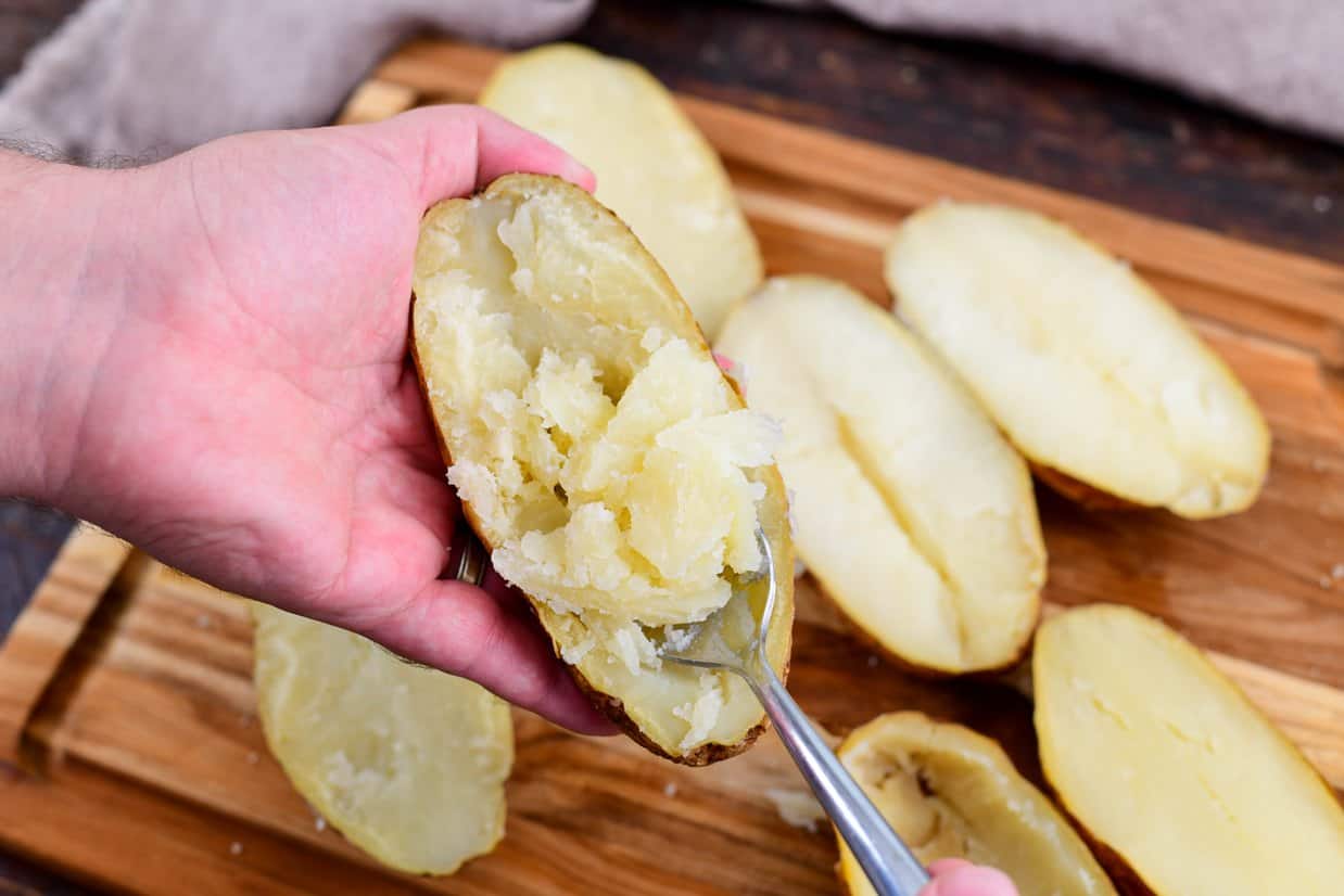 potato shells on a cutting board with a potato held while scooping meat out