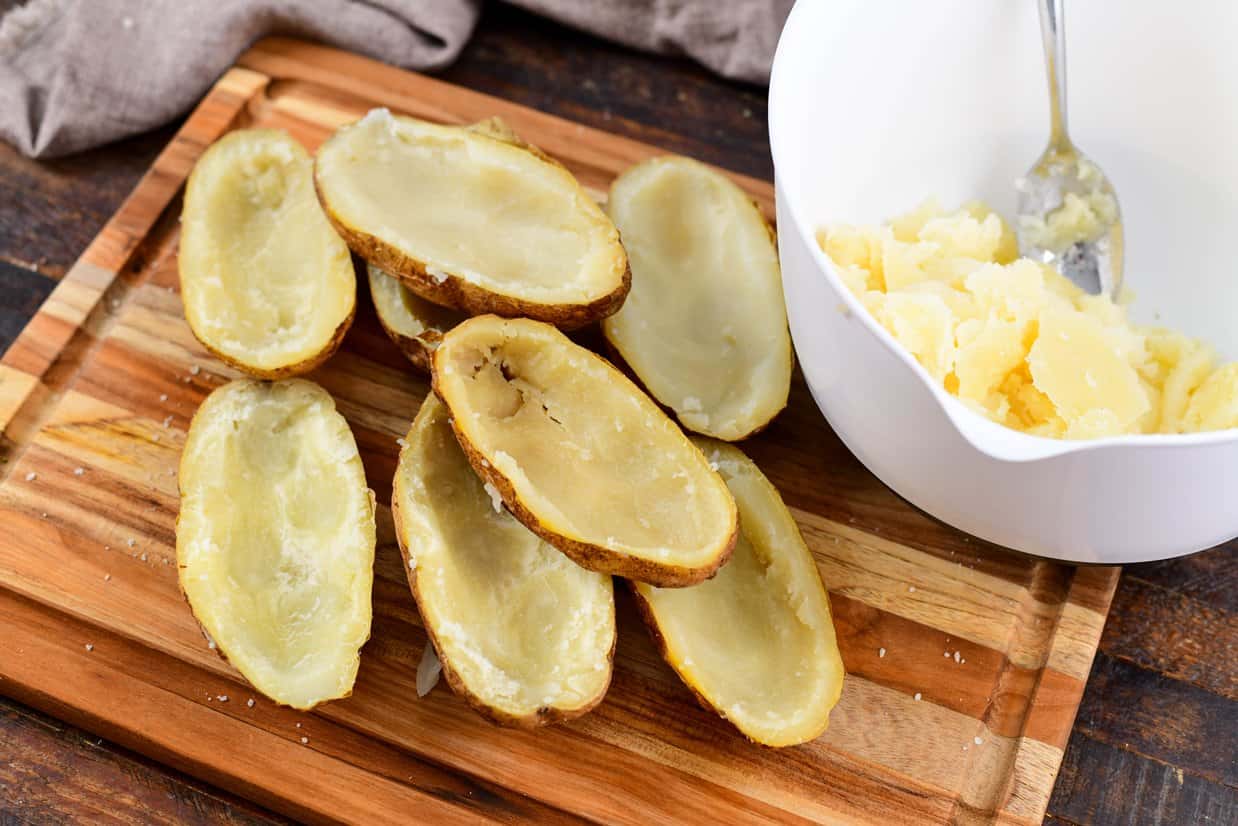 potato shells on a cutting board with potato meat in a white bowl