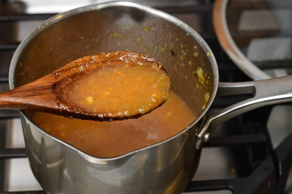 Spoon holding cooked sauce above a medium sauce pan.