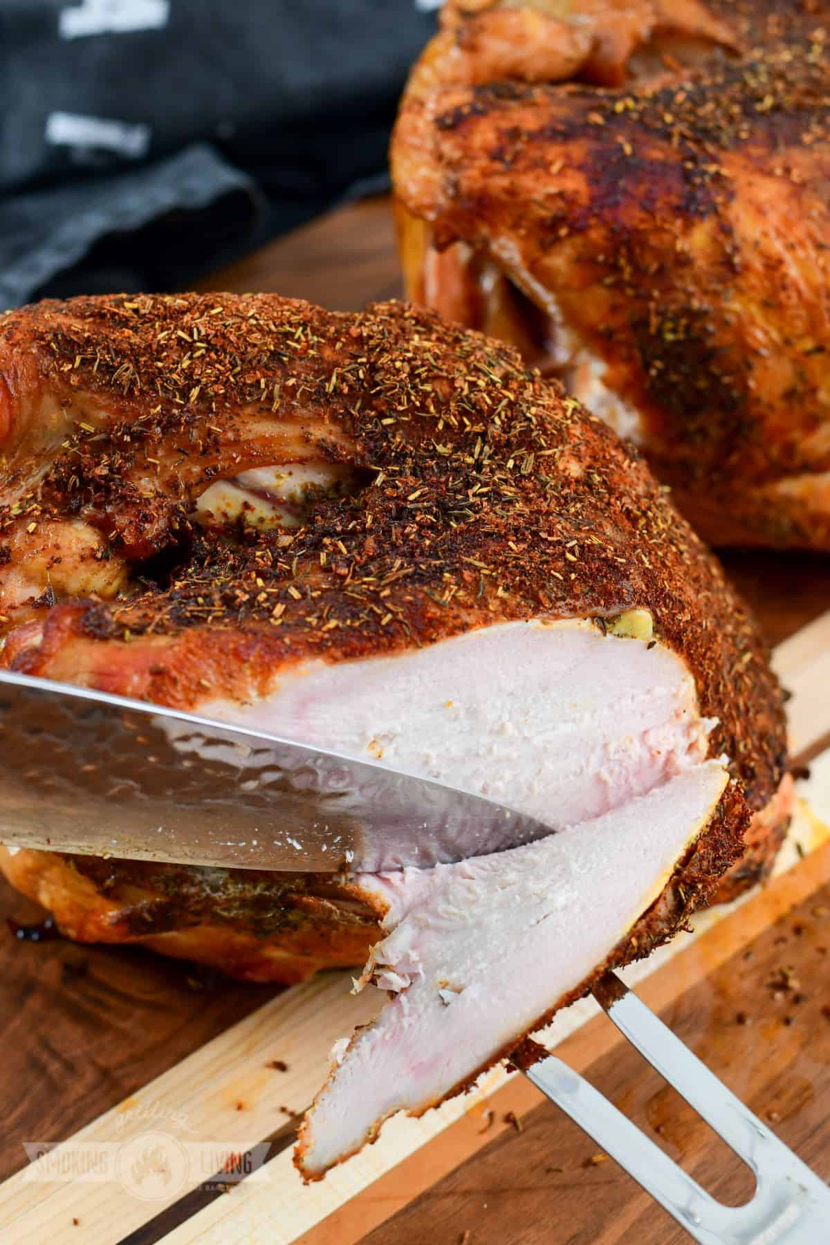 slicing smoked turkey breast with a knife and two prong fork.