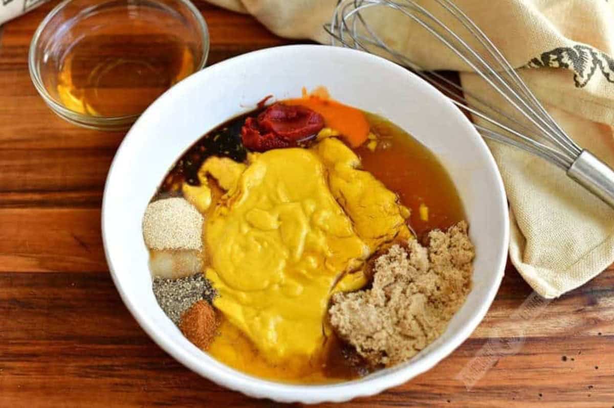 Ingredients for Carolina mustard sauce in a bowl on a wood surface and a whisk beside it.