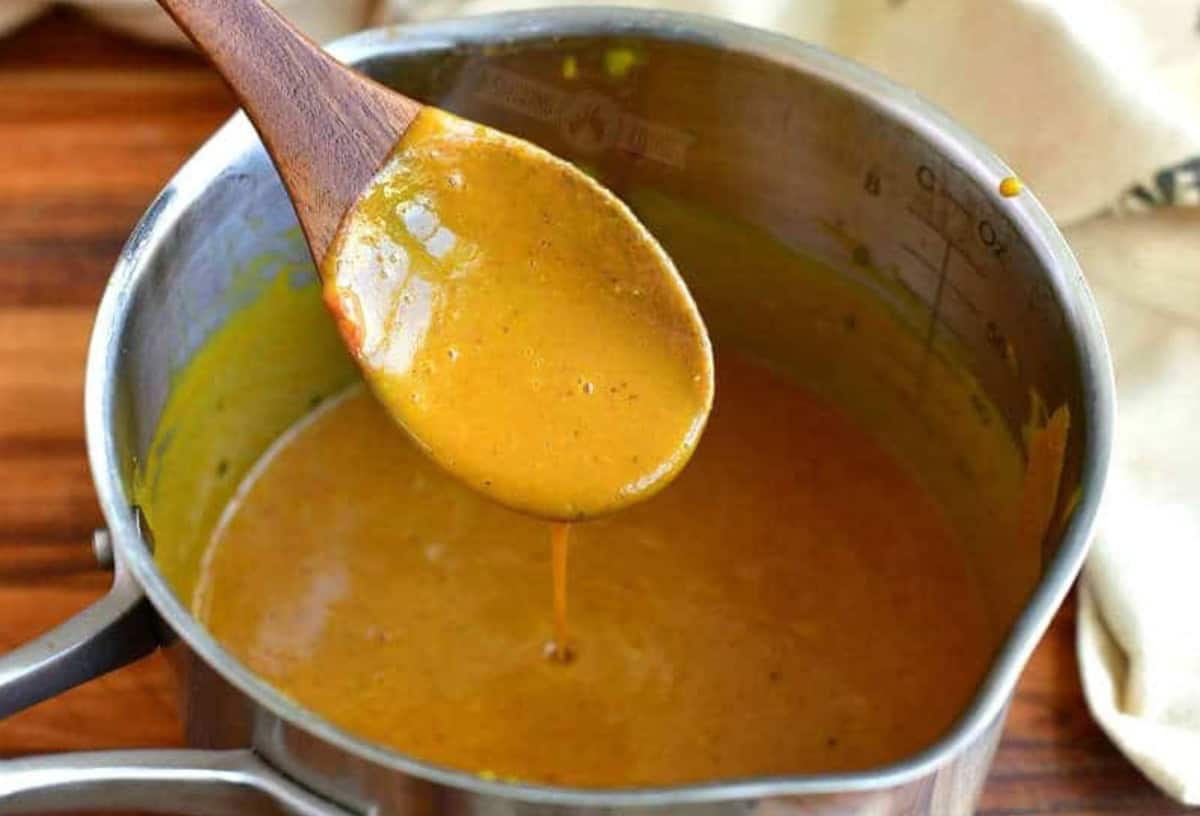 Carolina mustard sauce in a pot with some being scooped out with a wooden spoon.