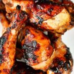 Grilled chicken legs marinaded and cooked stacked on a plate.