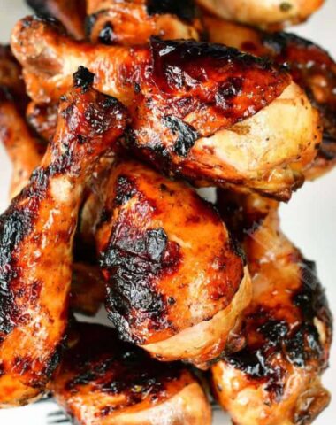 Grilled chicken legs marinaded and cooked stacked on a plate.